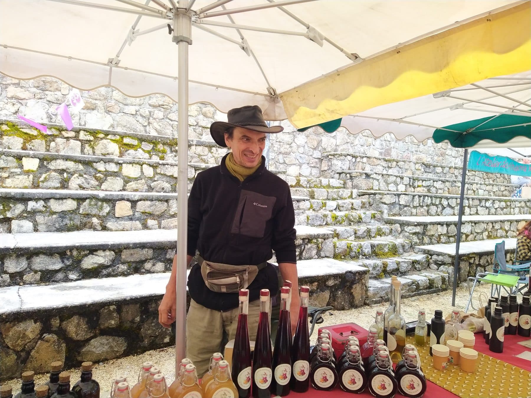 Frédéric sur un marché, devant ses bouteilles d'élixirs